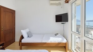 A bedroom with a wooden bed, a television mounted on the wall, and a large window offering a view of the sea. - Apartments Rosić Baošići (Baošici)