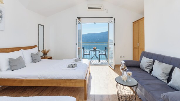 A bedroom with a bed, a sofa, a balcony with a table and chairs, and a view of the sea. - Apartments Rosić Baošići (Baošici)