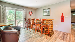 A room with a wooden floor, a sofa, a dining table, and several chairs. There is a window with curtains, a framed picture on the wall, and a red sign with the word "BAR" on it. - Wilmington Retreat Near Trails, Skiing & Festivals (Wilmington)