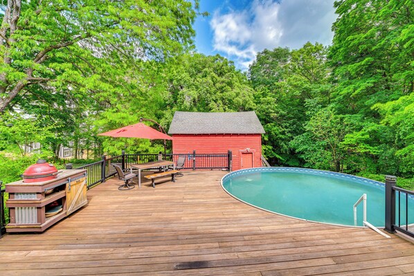 Um deck de madeira com piscina, um edifício vermelho e uma área de churrasco.