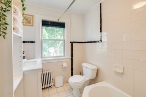 Un baño moderno con inodoro, lavamanos y bañera. Se ve un ventanal con vistas a árboles.