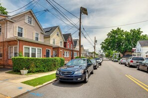 Una calle residencial con casas, coches aparcados y un seto.