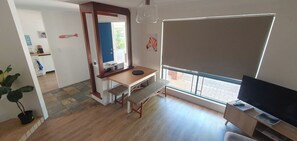Ein Zimmer mit Holzboden, einem Esstisch mit Bänken, einer TV-Kommode und einem großen Fenster.