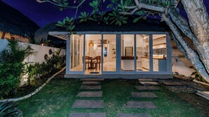 Una casa moderna con fachada de vidrio, techo de paja y jardín con losetas.