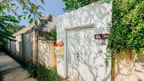 Una villa llamada "Villa Cinto" con fachada blanca, cerca de madera y techo de paja.