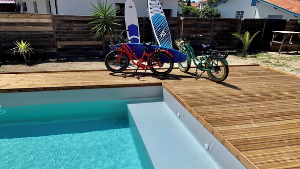 Ein Schwimmbad mit Holzterrasse, umgeben von einem Holzzaun und Palmen.