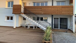 Ein modernes, zweistöckiges Haus mit einer Holzterrasse, einer Treppe und einem Balkon.