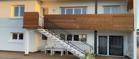 Una casa moderna de dos pisos con un porche de madera, una escalera y un balcón.