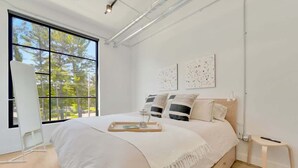 A modern bedroom with a large window, a bed with a tray, and two wall-mounted artworks. - 1BR Condo I King Bed + Sofa I Near DT TC (Traverse City)