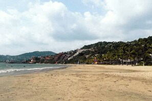 A beach with a sandy shore, a few buildings in the background, and palm trees lining the beach.