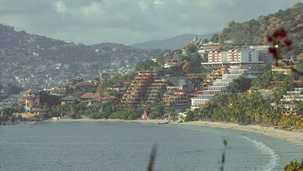 Un paisaje costero con playa, edificios residenciales y colinas al fondo.