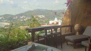 Una terraza con mesa y sillas, con vistas a un paisaje costero con colinas y edificios.