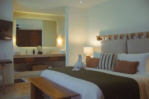 Ein Hotelzimmer mit Bett, Nachttisch, Bank und einem Badezimmer mit Waschtisch und Spiegel.