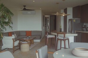 A modern living room with a sofa, coffee table, and chairs, a dining area with a table and chairs, and a kitchen with cabinets and appliances.
