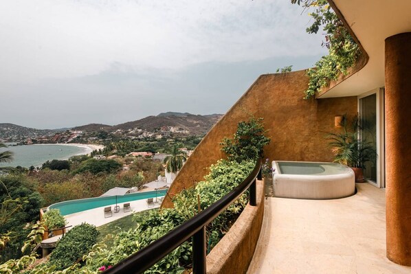 Un balcon avec un jacuzzi, une piscine et une vue sur une plage et des collines.
