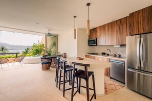 Une cuisine moderne dotée d’un grand îlot central, d’appareils électroménagers en acier inoxydable et offrant une vue sur l’extérieur.