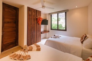 Een hotelkamer met twee bedden, een houten deur, een televisie op een plank en een raam met uitzicht op groen.
