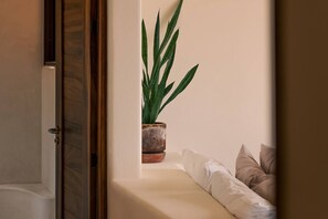 Een hoek van een kamer met een potplant, een houten deur en een witte bank met kussens.
