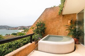 A balcony with a hot tub, a view of the sea, and a hillside.