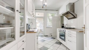Cozinha moderna com armários brancos, fogão a gás, forno e uma grande janela que traz luz natural.