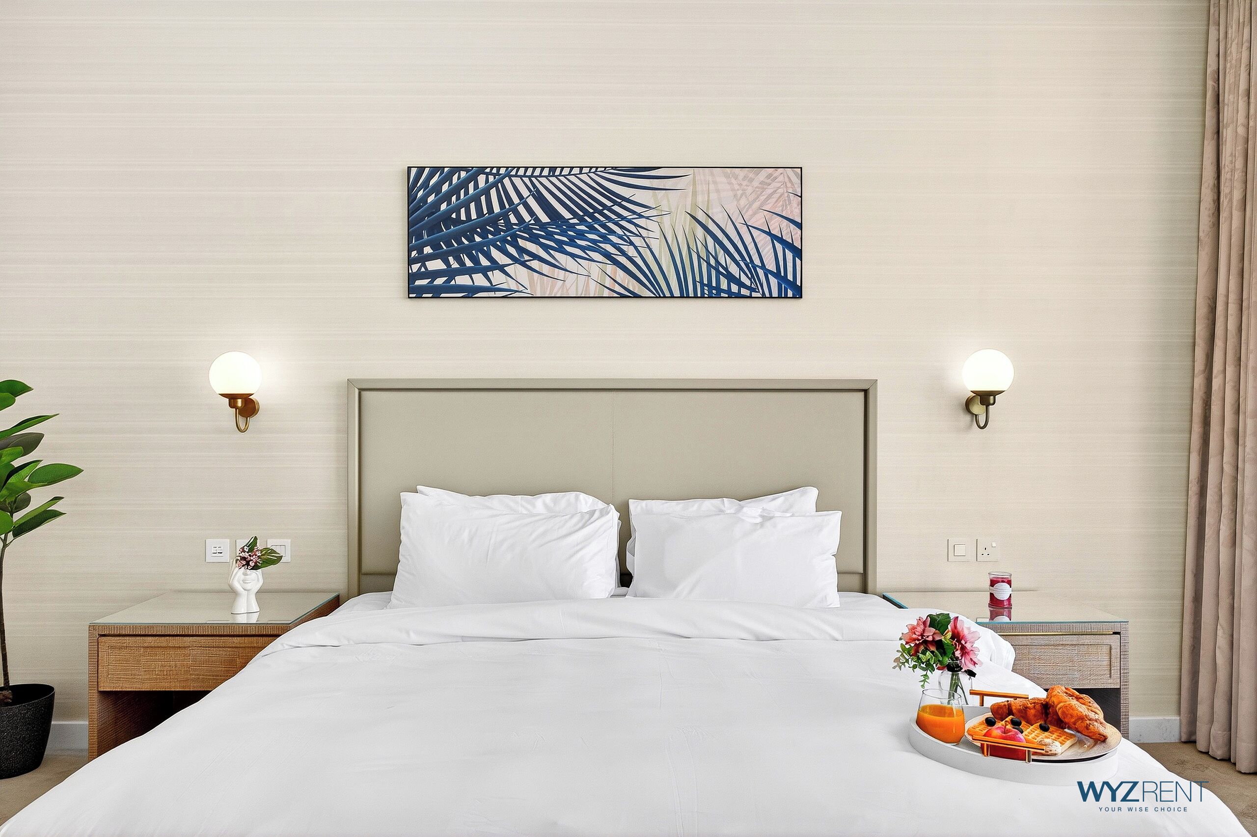 A neatly made bed with white linens, a wall-mounted abstract painting, bedside lamps, and a breakfast tray on the nightstand.
