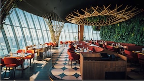 A modern restaurant with a high ceiling, large windows, and a circular seating area. - WYZ RENT|Palm Tower 1 BD Nakheel Mall High Floor (Dubai)
