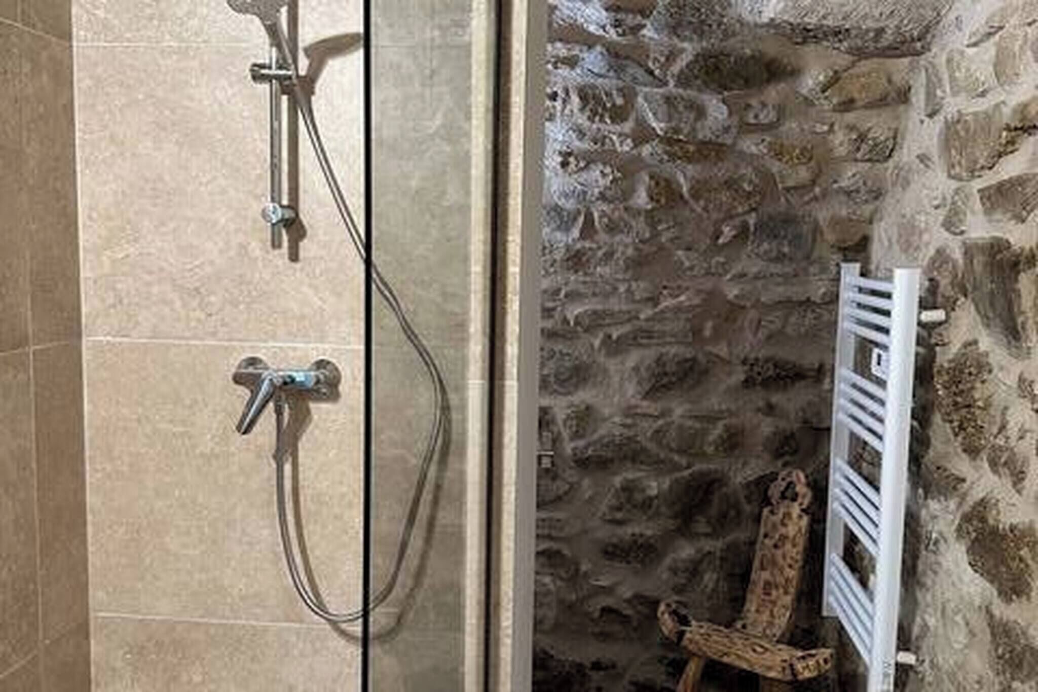 A bathroom with a stone wall, a shower with a handheld showerhead, and a towel rack.