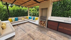 An outdoor patio with a built-in grill, seating area, and a sink.