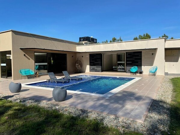 A modern house with a swimming pool, outdoor seating, and a garage.