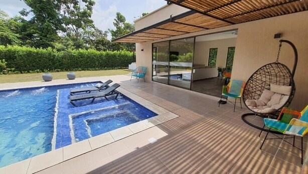 A modern outdoor pool area with lounge chairs, a hanging chair, and a glass-enclosed patio.