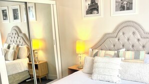 Un lit bien fait, recouvert d’une couvre-lit à motifs, avec deux lampes de chevet et un miroir qui reflète la pièce.