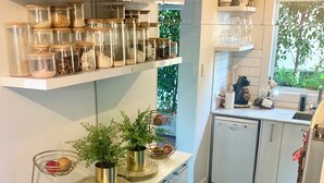 Une cuisine moderne avec des meubles blancs, un plan de travail en granit et divers appareils de cuisine. On y trouve des étagères avec des bocaux en verre et une plante en pot sur le plan de travail.