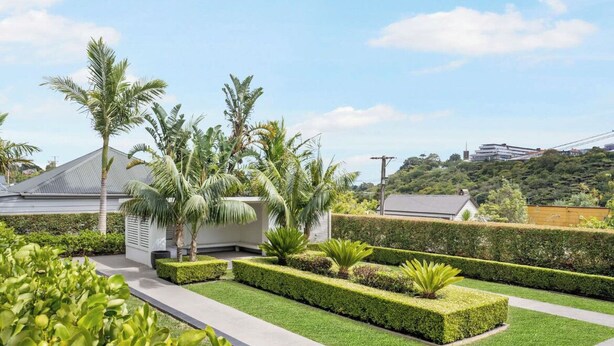 Un jardin aménagé avec des haies taillées, des palmiers et un sentier.