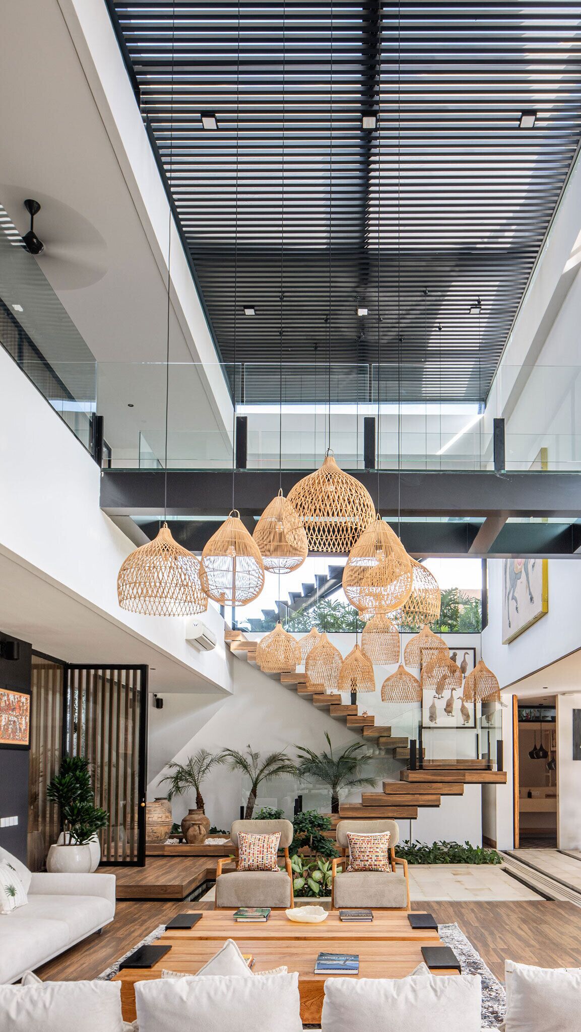A spacious, modern interior with a high ceiling, a staircase, and multiple hanging wicker lamps.