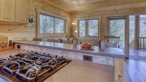 Cocina de cabaña de madera con estufa a gas, ventanas amplias y una zona de comedor.