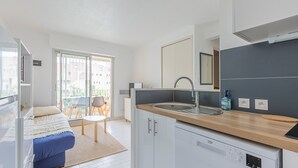 Una cocina compacta con lavavajillas integrado, un lavamanos y una ventana con vistas a un balcón.