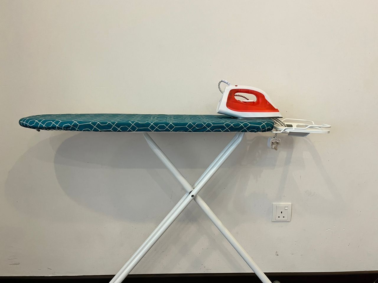 An ironing board with a teal patterned cover and a red and white iron.