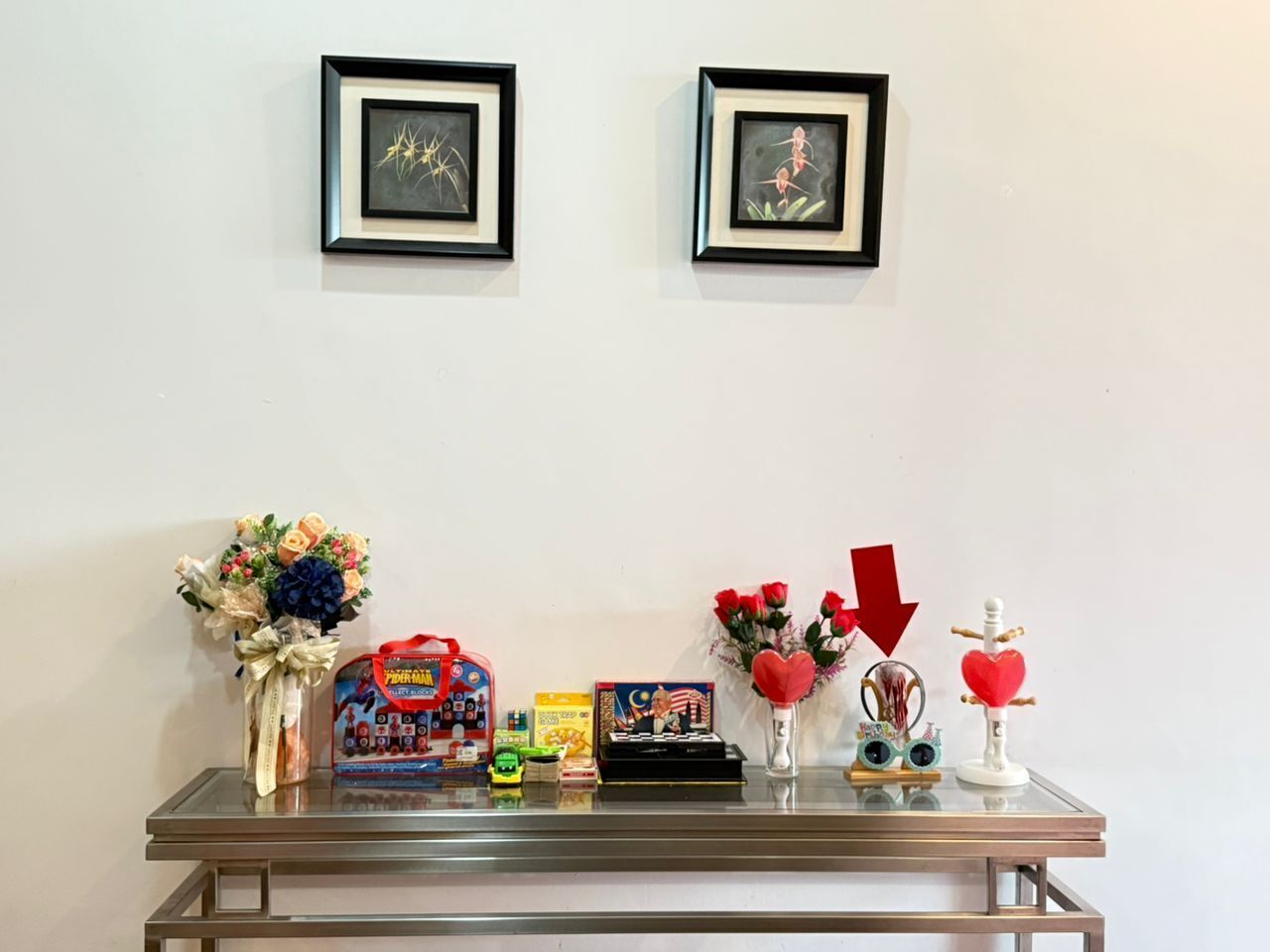 A display table with framed artwork, a bouquet of flowers, a toy car, a gift box, and a small figurine.