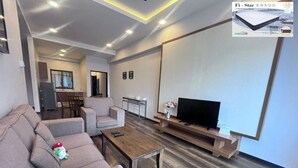 Ein modernes Wohnzimmer mit Sofa, Couchtisch, TV-Möbel und einem Essbereich im Hintergrund.