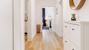 Un couloir doté d’un plancher en bois, de murs blancs et d’un grand miroir sur le côté droit.