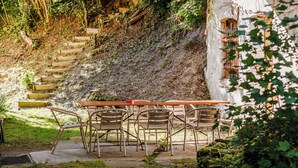 Un espace extérieur aménagé dans un style rustique, avec une table et des chaises, entouré de verdure et agrémenté d’un escalier en pierre.