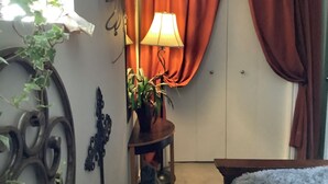 Een kamer met een lamp op een klein tafeltje, een bloempot en een raam met gordijnen.