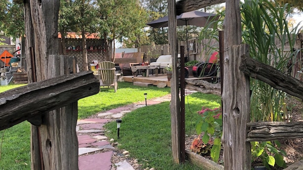 Een rustieke buitenruimte met een houten pergola, een pad van stenen en buitengemeubilair.