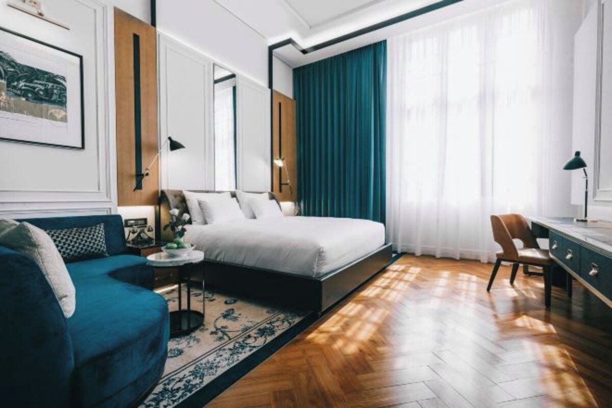 A modern hotel room with a bed, a desk, a chair, a sofa, and a small table.
