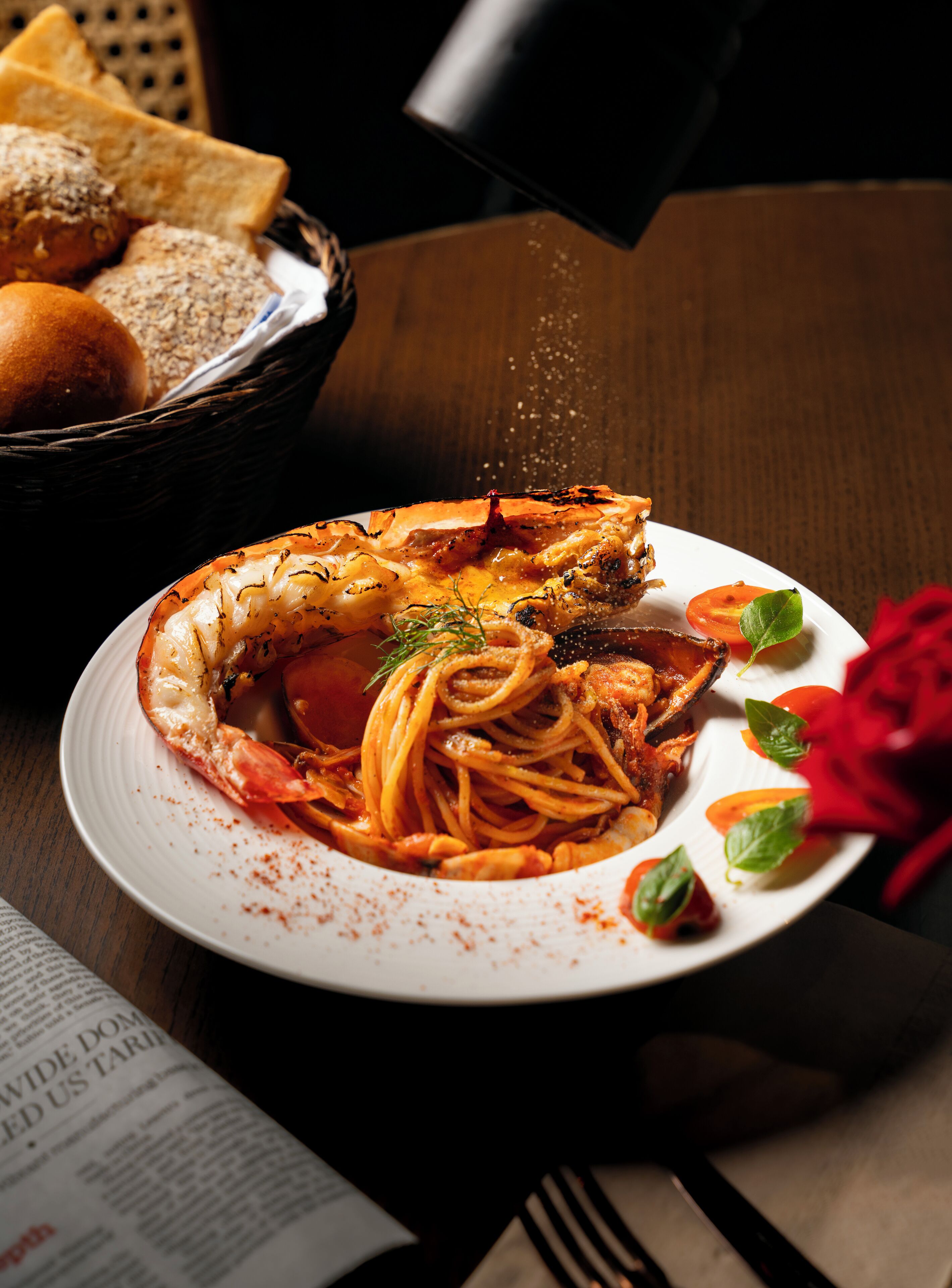 A plate of spaghetti with a lobster tail, garnished with herbs, and a red rose.