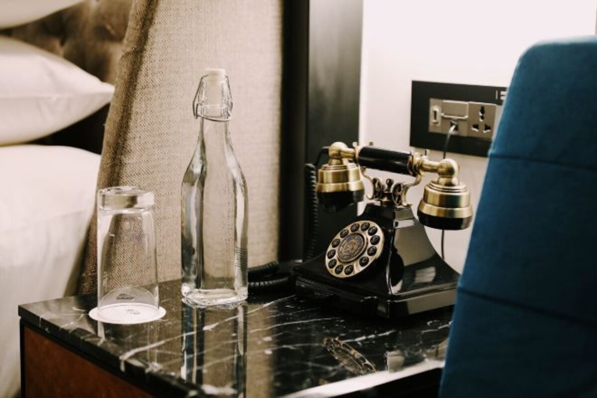 A hotel room with a marble bedside table, a vintage rotary phone, and two clear glass bottles.