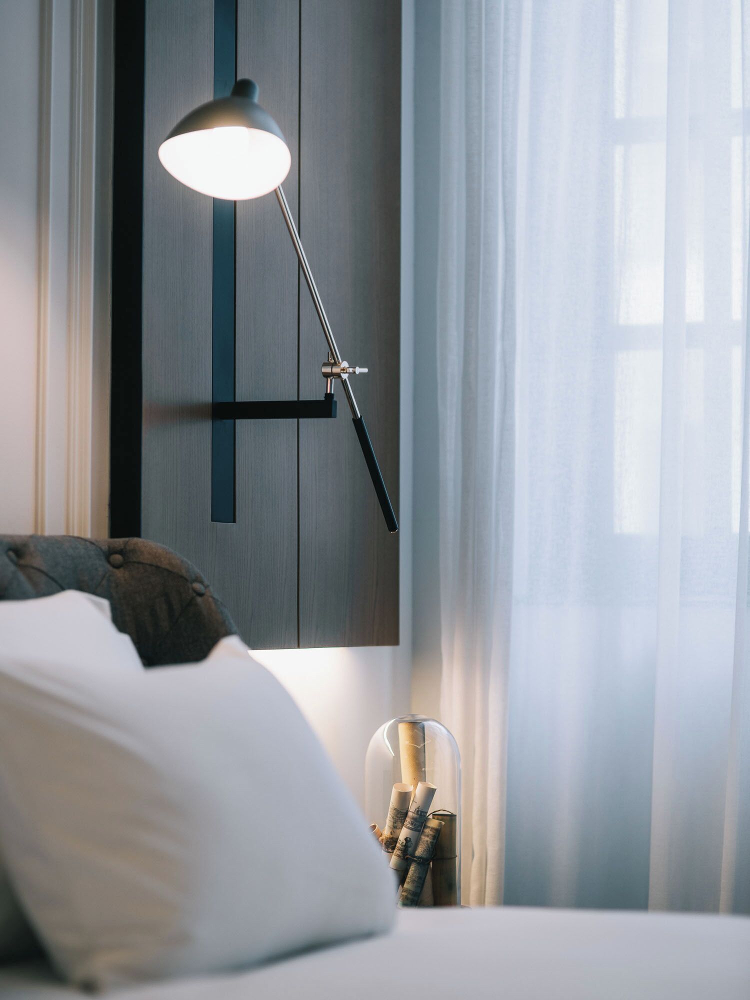 A modern bedroom with a bed, a bedside lamp, a nightstand, and a glass container with rolled-up papers.