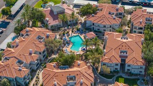 Vue aérienne d’un quartier résidentiel composé de plusieurs immeubles aux toits recouverts de tuiles rouges, avec une piscine centrale et de nombreux espaces verts environnants.