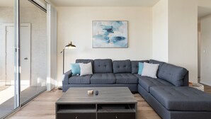 Un salon moderne avec un canapé d’angle, une table basse et un grand tableau abstrait accroché au mur.