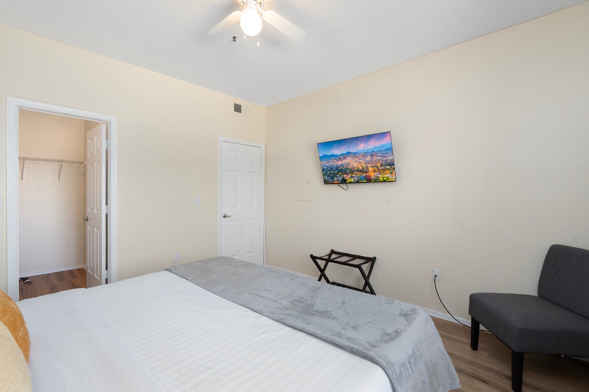 A bedroom with a bed, a chair, a TV, and a door leading to a closet.
